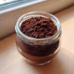 Close-up of rich brown homemade hot cocoa mix powder filling a small glass jar.