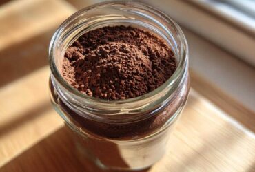 Close-up of rich brown homemade hot cocoa mix powder filling a clear glass jar.