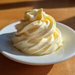 A beautiful swirl of creamy, pale yellow homemade mayonnaise piped onto a small white saucer.