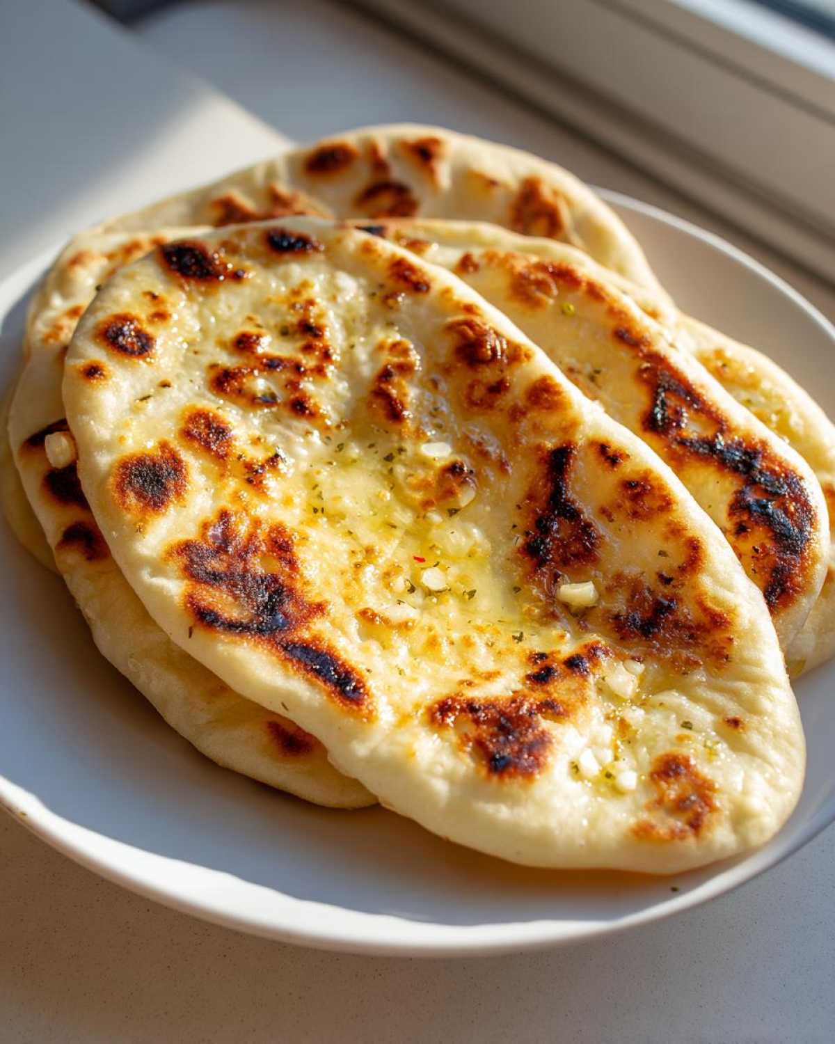 A stack of freshly made homemade naan bread brushed with melted garlic butter and herbs.