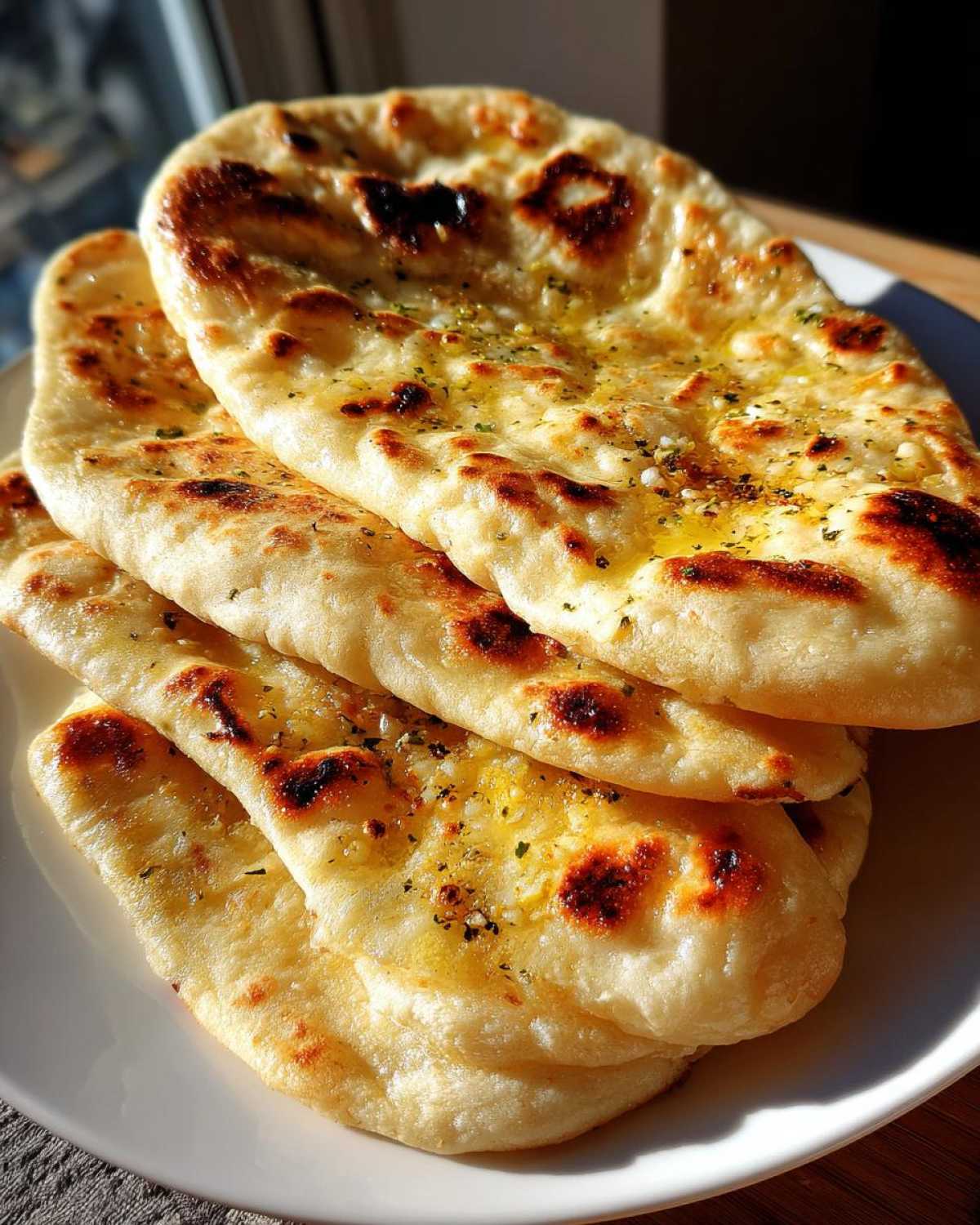 A stack of four fluffy, golden homemade naan bread pieces brushed with melted butter and herbs.