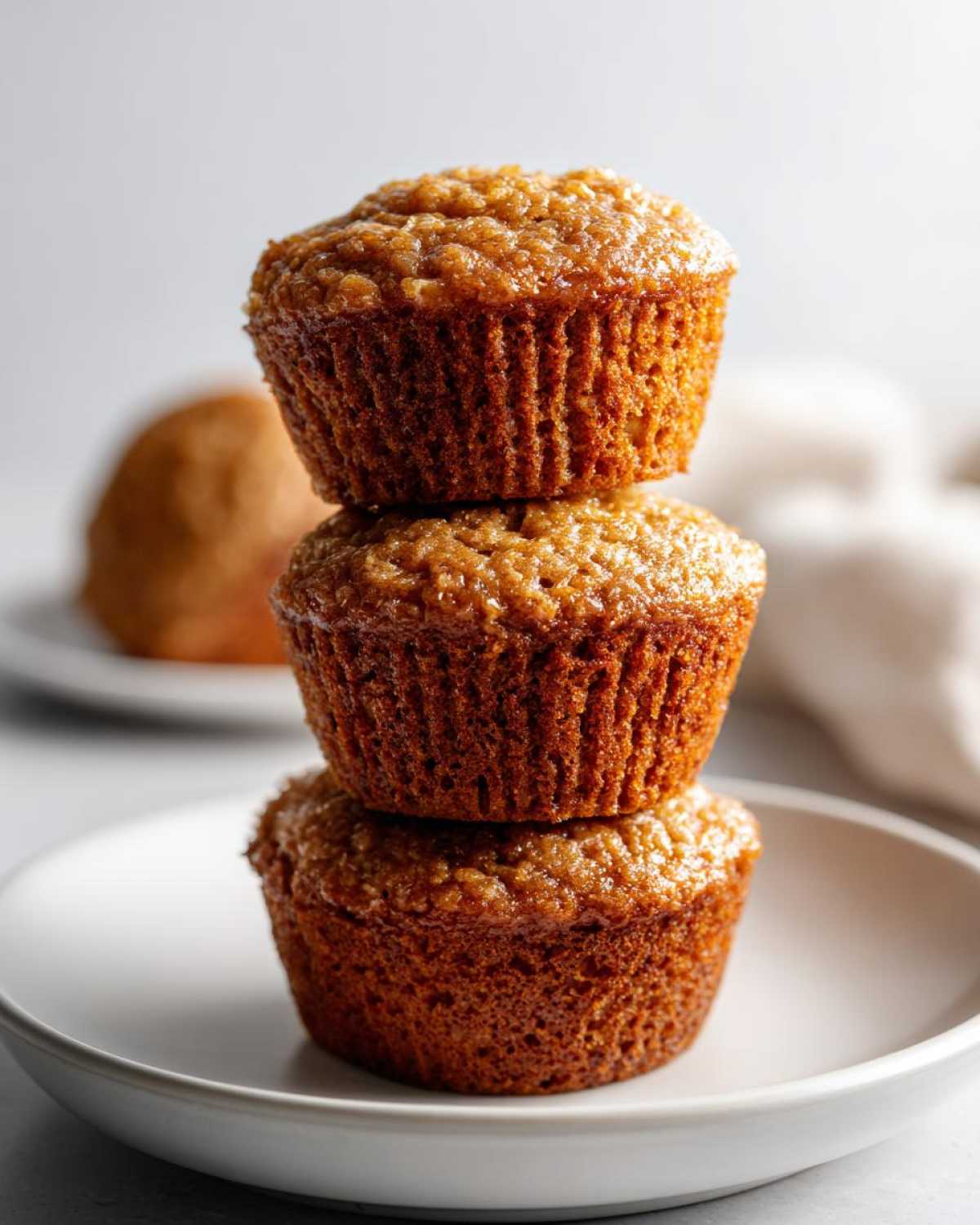 Three freshly baked honey bran muffins stacked vertically on a small white plate.
