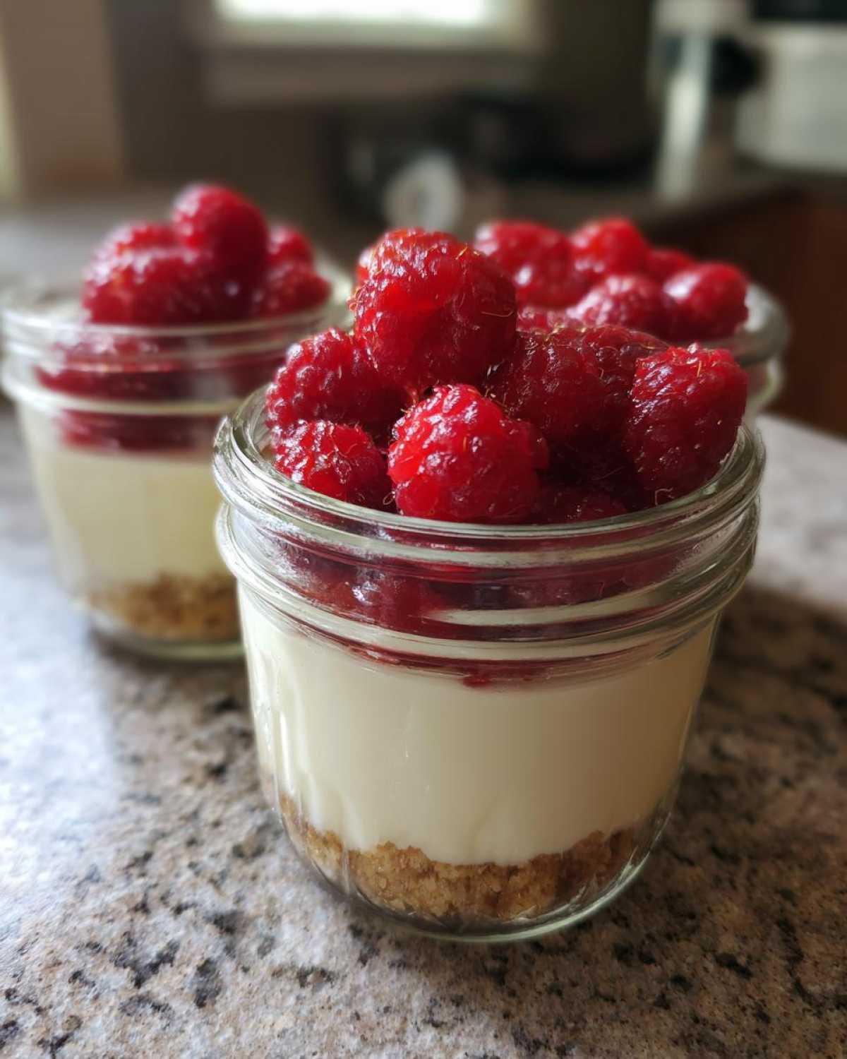 Close-up of individual Protein Cheesecake servings in small glass jars topped with fresh raspberries.