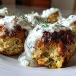 Close-up of several juicy greek chicken meatballs topped with creamy tzatziki sauce and fresh dill.