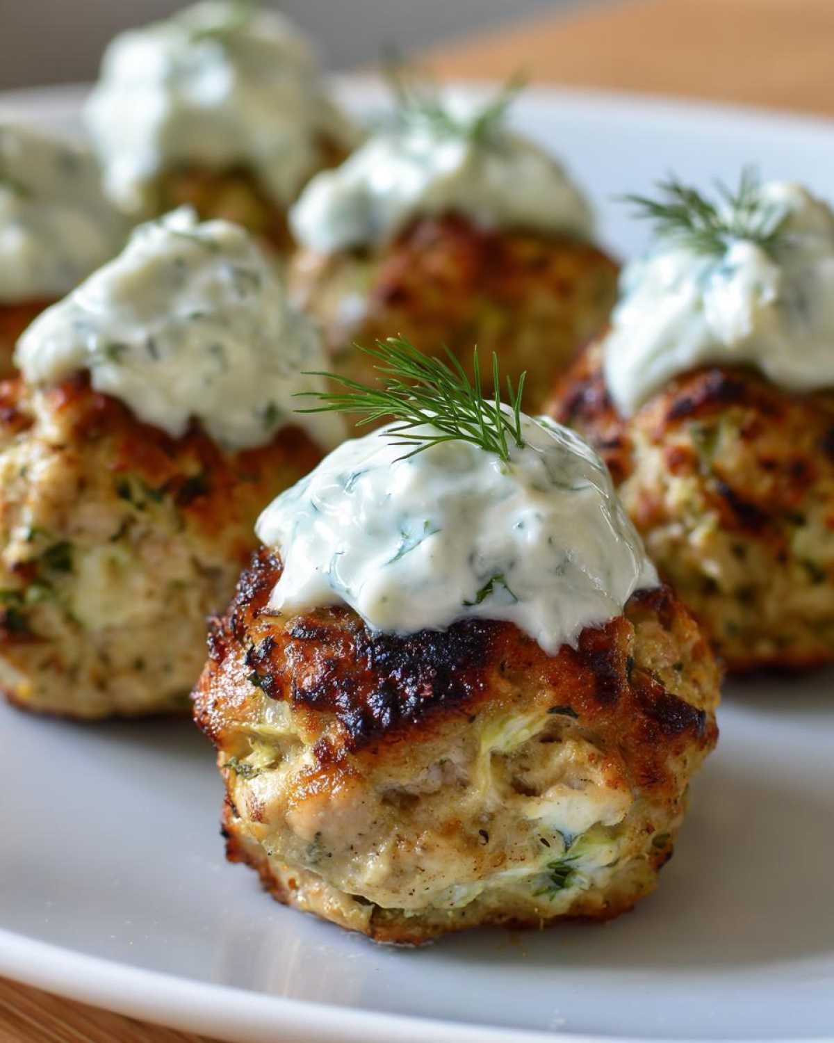 Close-up of perfectly browned greek chicken meatballs topped with creamy tzatziki sauce and fresh dill.