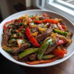 Close-up of juicy steak fajitas with colorful bell peppers and onions served in a white bowl.