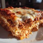 A close-up, sunlit slice of Lasagna with Cottage Cheese showing layers of meat sauce, pasta, and melted cheese topping.