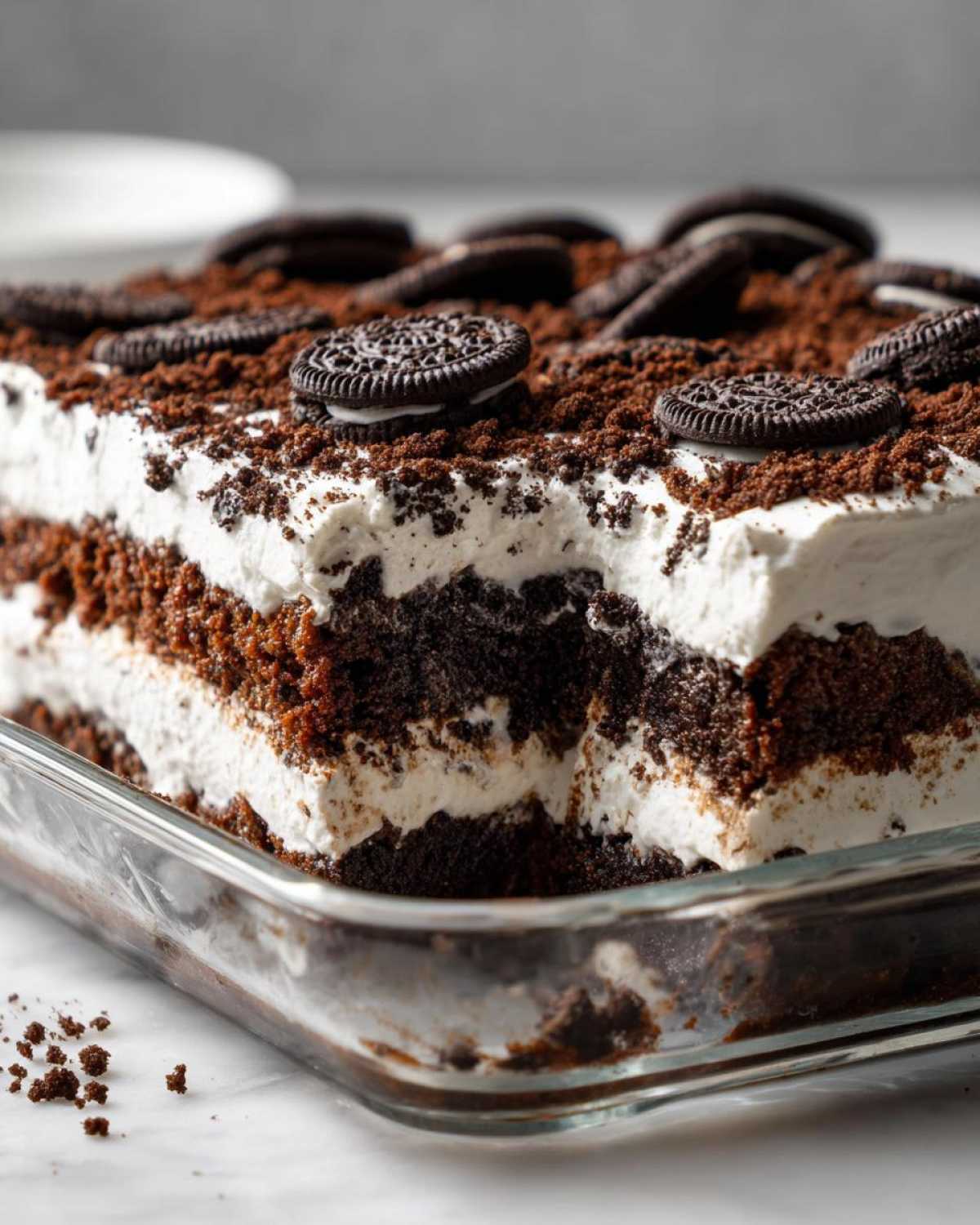 A close-up view of a layered oreo dirt cake in a glass baking dish, showing chocolate cake, cream filling, and Oreo cookie topping.