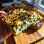 A hand holding a golden-brown slice of Mediterranean Spinach and Feta Cheese Crisps, showing rich spinach and white feta filling.