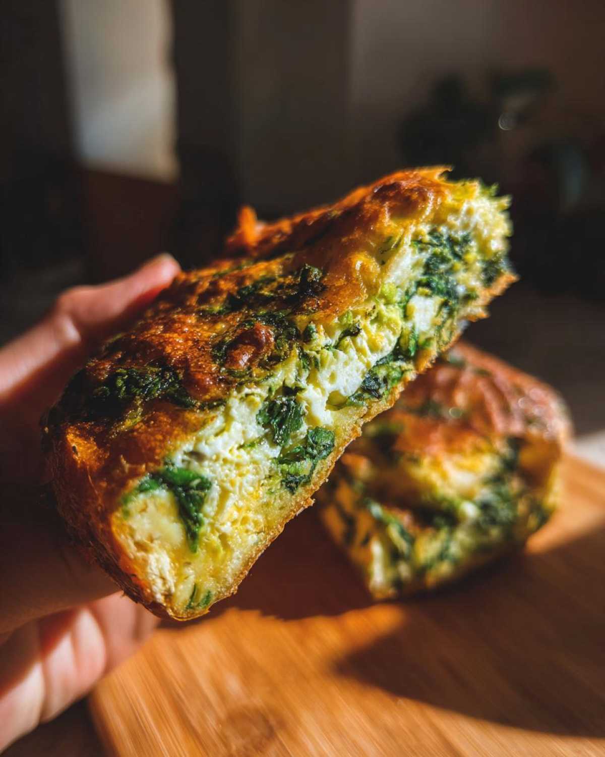 A hand holds up half of a golden-brown Mediterranean Spinach and Feta Cheese Crisps, showing the fluffy interior with spinach and feta.