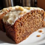 Close-up of two slices of moist, dark brown applesauce cake topped with thick, creamy white frosting.