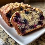 Close-up of a moist slice of blueberry banana bread showing rich blueberries and a crumbly streusel topping.