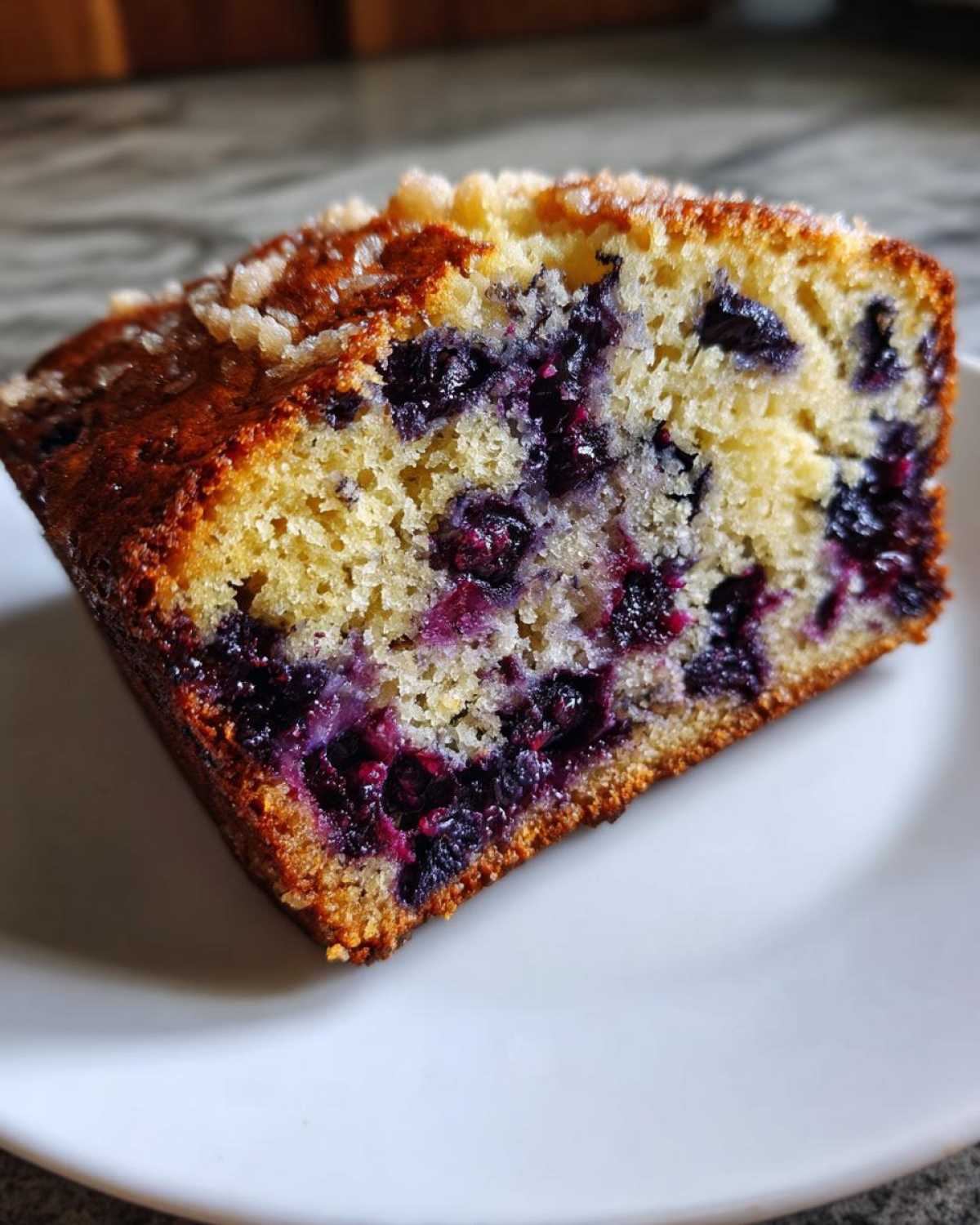 Close-up of a moist slice of blueberry banana bread showing vibrant purple blueberries baked into the yellow crumb.