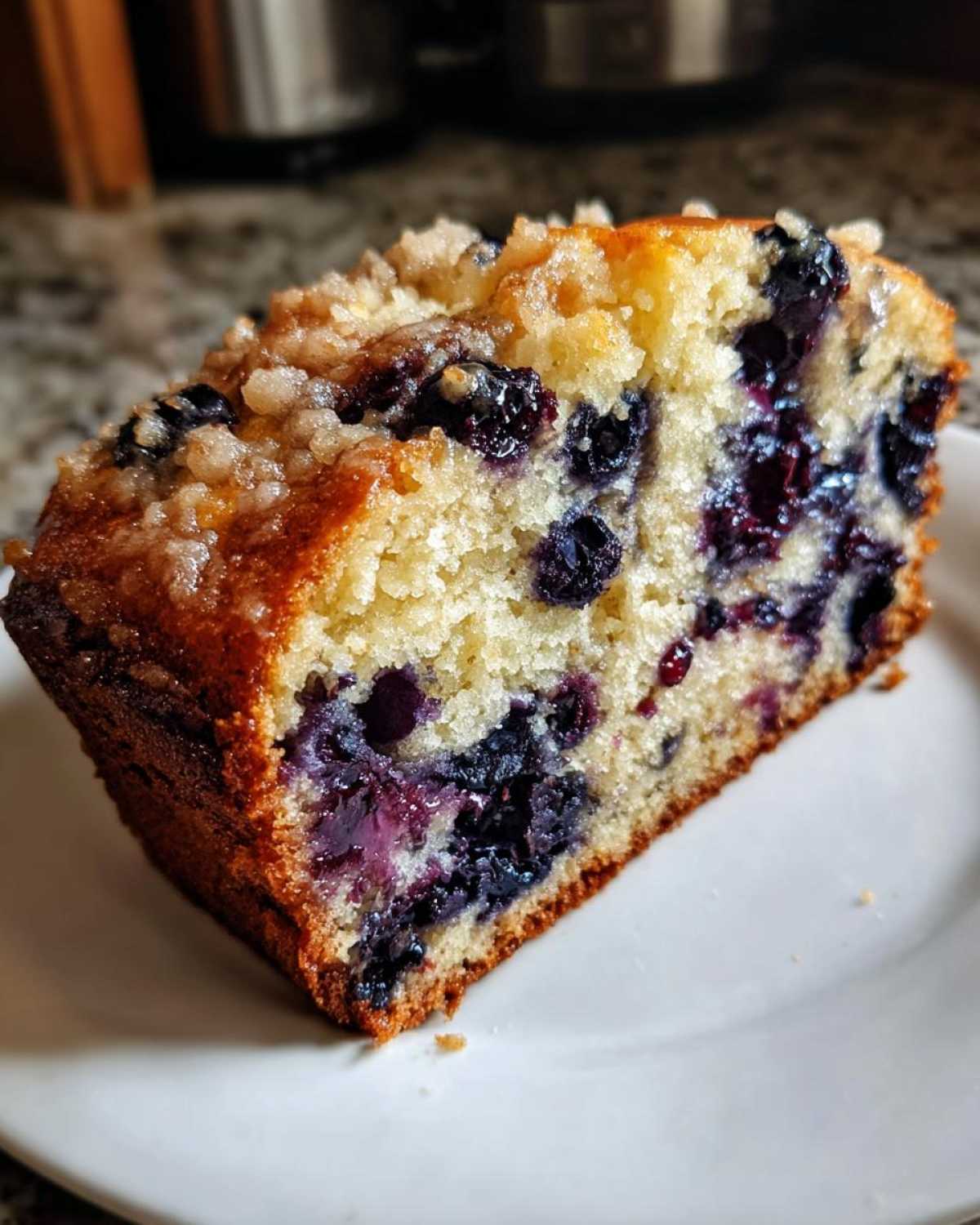 Close-up of a moist slice of blueberry banana bread featuring bursting blueberries and a sugary streusel topping.