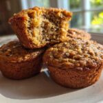 A stack of three moist bran muffins, one broken open to show the texture.