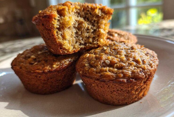 A stack of three moist bran muffins, one broken open to show the texture.