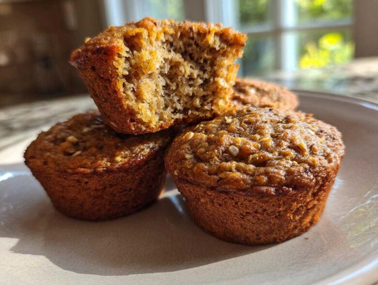 A stack of three moist bran muffins, one broken open to show the texture.