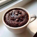 Close-up of a moist chocolate mug cake topped with melted chocolate chips, ready to eat.