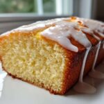 Close-up of a moist lemon pound cake loaf, sliced to show texture, topped with thick white lemon glaze dripping down the sides.