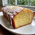 A close-up of a slice of moist lemon pound cake topped with white glaze and lemon zest.