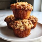 A stack of three moist oatmeal muffins featuring a thick, golden brown crumb topping, served on a white plate.