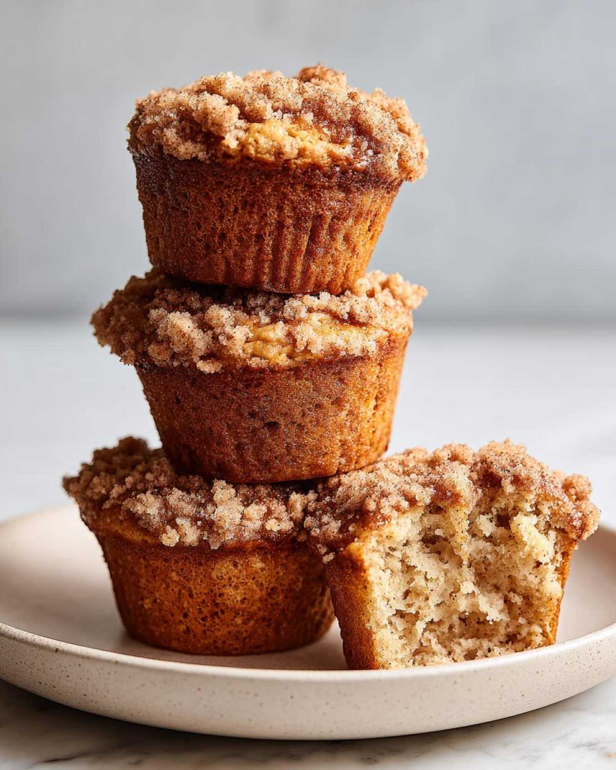 A stack of three moist oatmeal muffins topped with cinnamon streusel, with one muffin broken open.