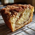 Close-up of a moist slice of sour cream coffee cake showing the cinnamon swirl and crumbly streusel topping.