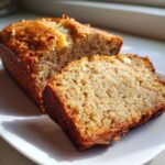A close-up of a slice cut from a loaf of moist sugar free banana bread, showing its texture and golden crust.