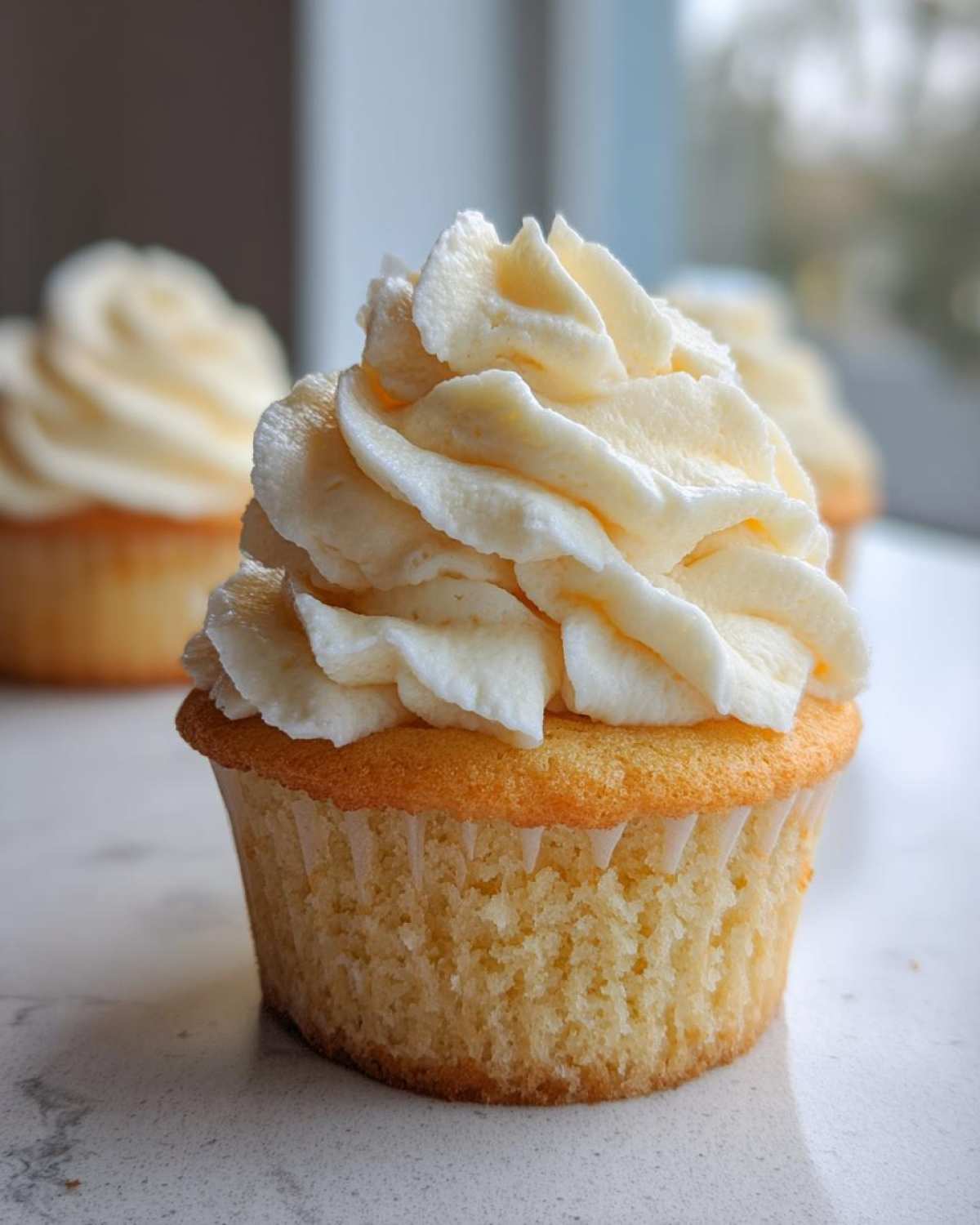 Close-up of a single, moist vanilla cupcakes topped with a generous swirl of creamy white frosting.
