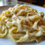 Close-up of fettuccine pasta generously coated in creamy Olive Garden Alfredo Sauce and topped with grated Parmesan.