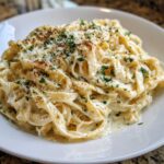 A close-up of fettuccine pasta generously coated in creamy Olive Garden Alfredo Sauce, topped with Parmesan and parsley.
