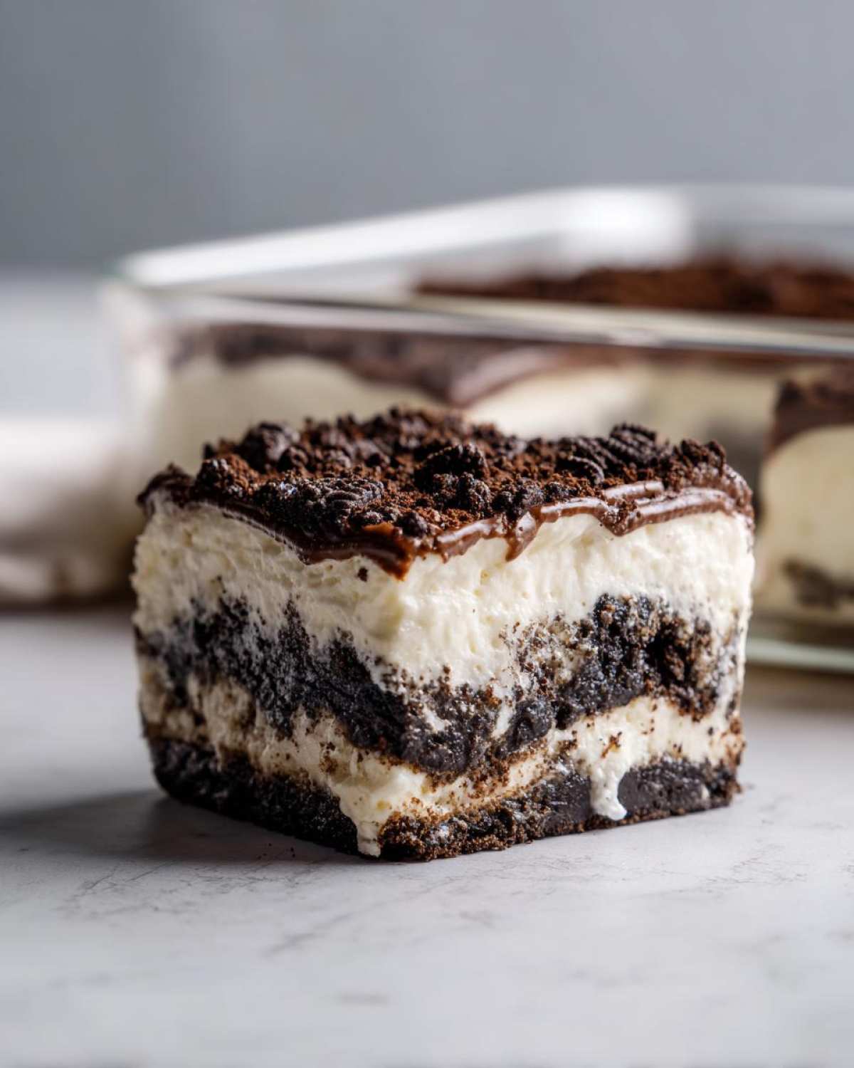 A close-up of a layered slice of oreo dirt cake featuring a dark cookie crust, creamy filling, and chocolate topping with cookie crumbles.