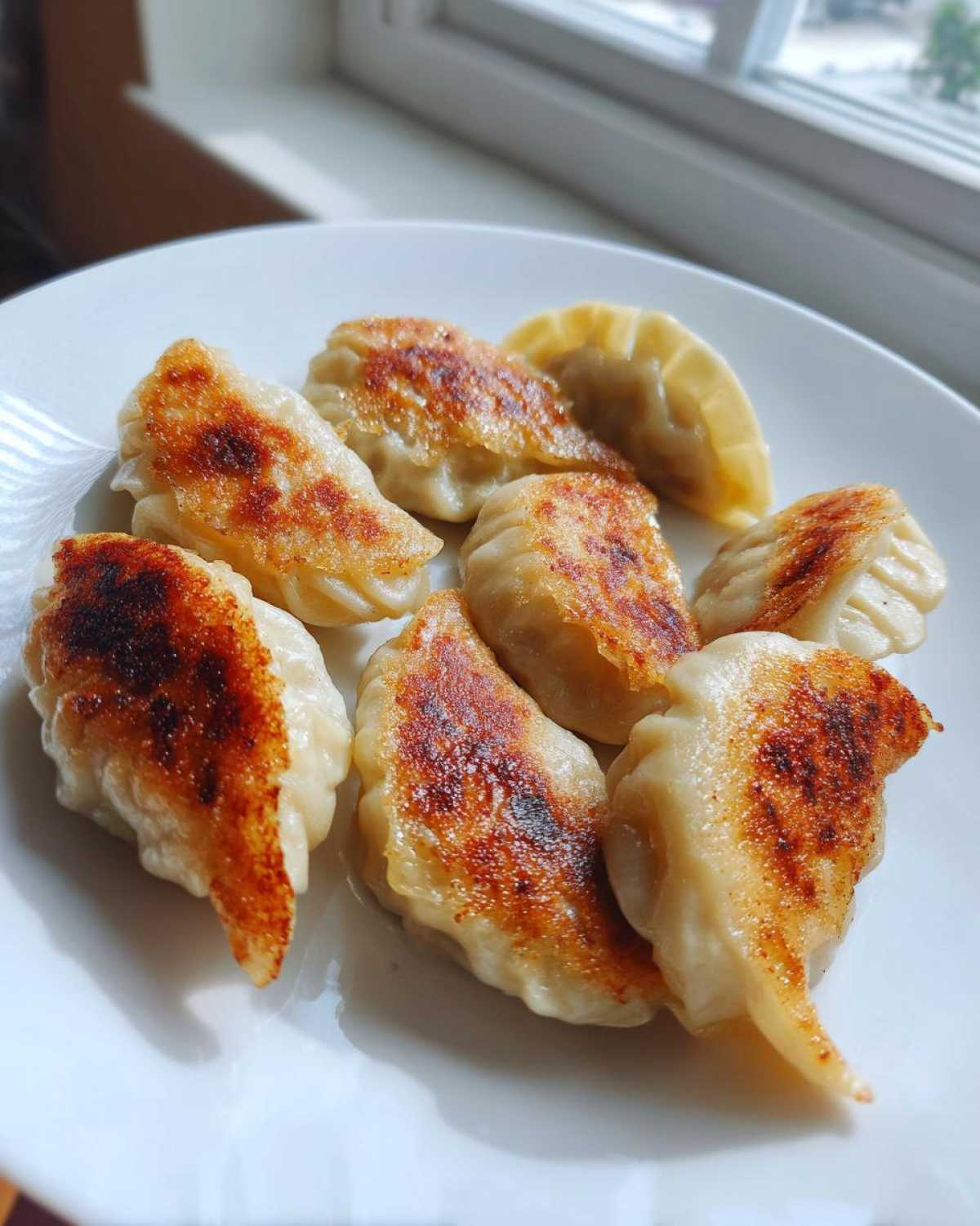 A close-up of several pan-fried Traditional Chinese Dumplings with golden-brown, crispy bottoms served on a white plate.