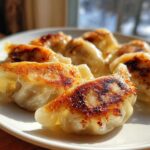 Close-up of several perfectly pan-fried Traditional Chinese Dumplings with golden-brown crispy bottoms on a white plate.