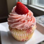 A single, beautifully frosted strawberry cupcakes topped with a fresh, whole strawberry.