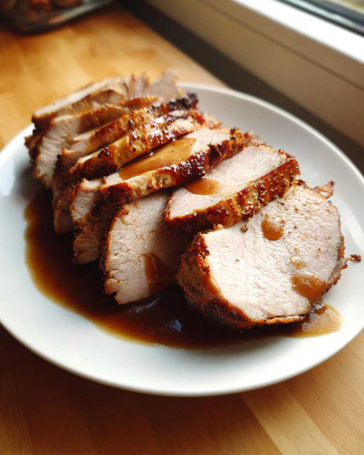 Slices of juicy pork loin roast, perfectly cooked and drizzled with rich brown gravy, served on a white plate.