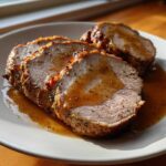 Close-up of three juicy slices of perfectly cooked pork loin roast drizzled with savory brown gravy on a white plate.