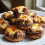 A pile of golden-brown sausage stuffed mushrooms topped with bubbly, melted cheese served on a white plate.