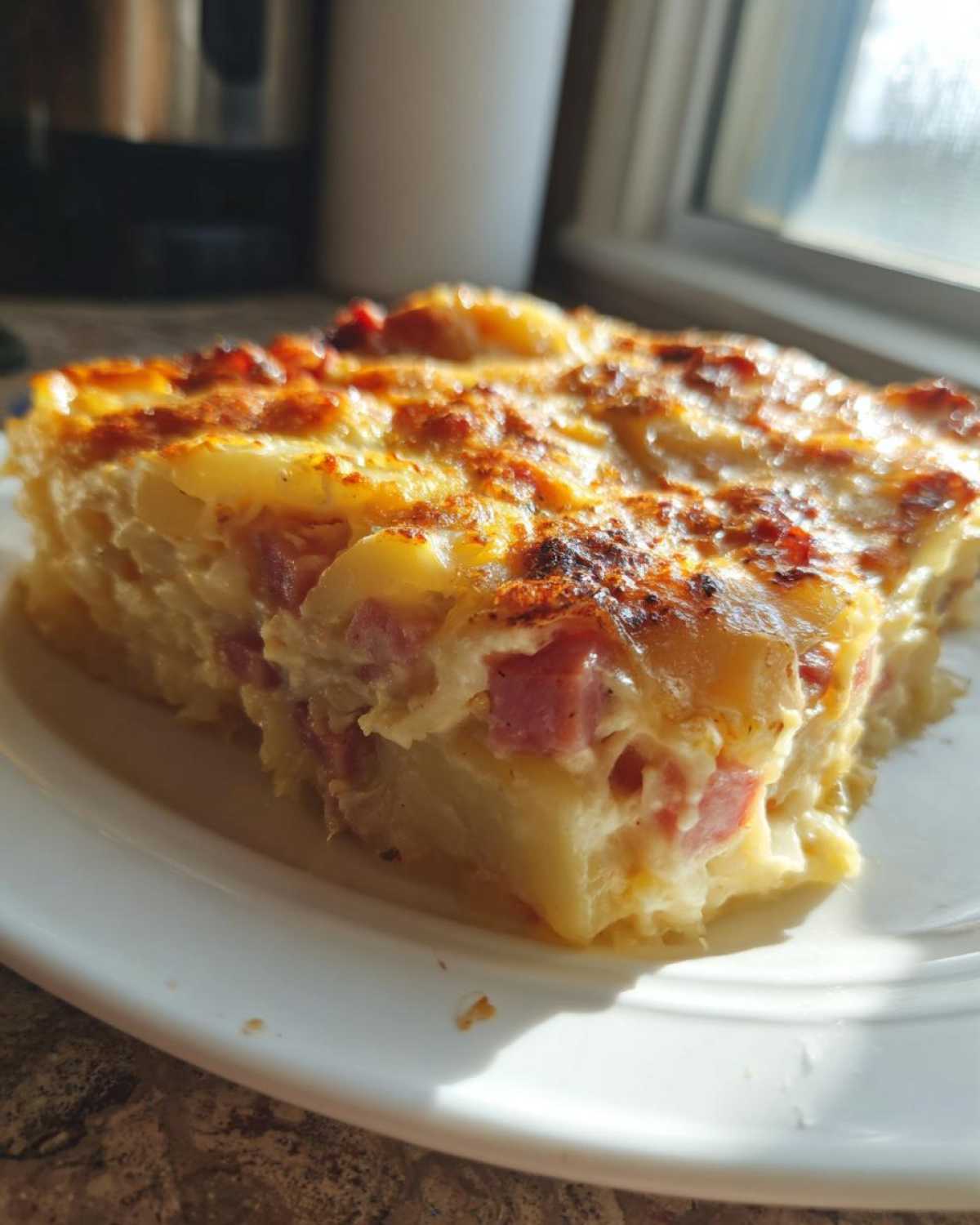 A close-up of a square slice of creamy scalloped potatoes and ham with a golden-brown, cheesy crust.