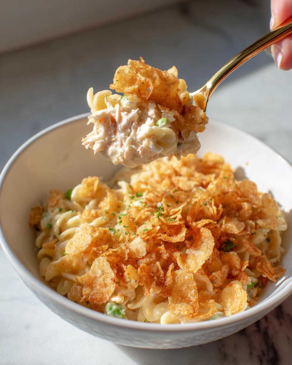 A spoonful of creamy Tuna Casserole topped with crispy flakes being lifted from a white bowl.