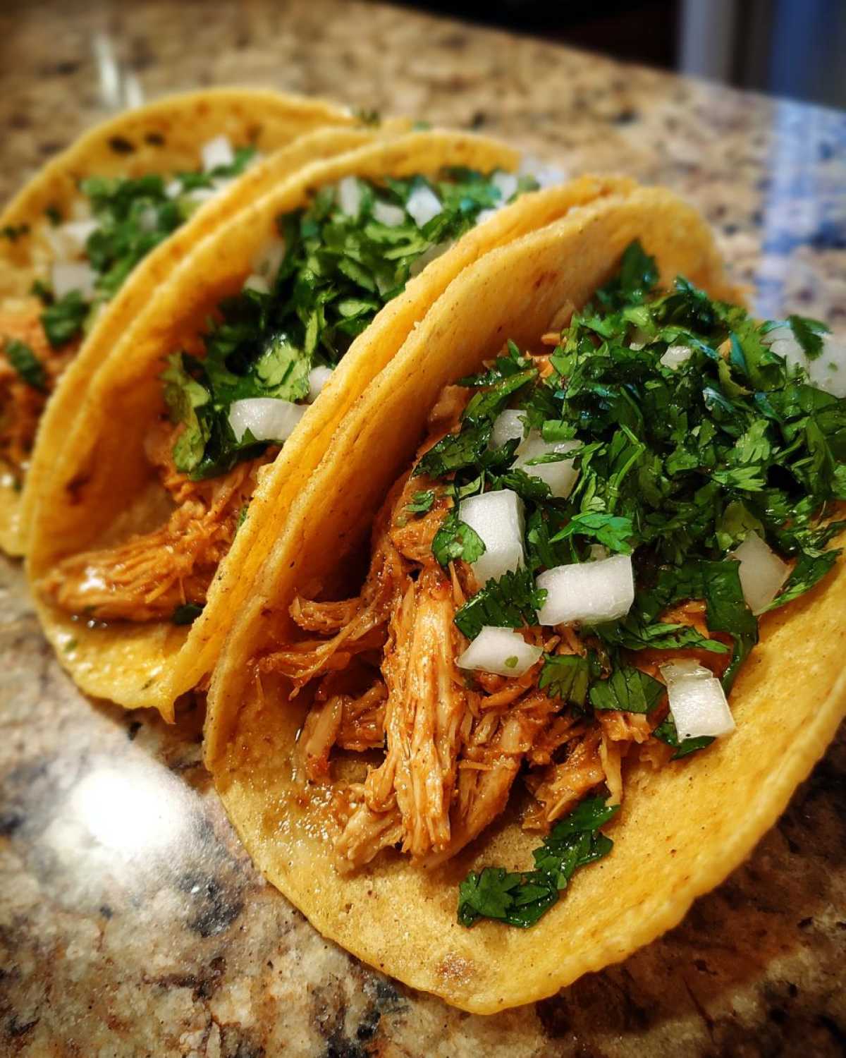 Three delicious chicken tacos filled with shredded seasoned chicken, topped with fresh cilantro and diced white onion.