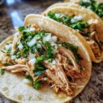 Close-up of authentic shredded chicken tacos topped with fresh diced onion and cilantro.