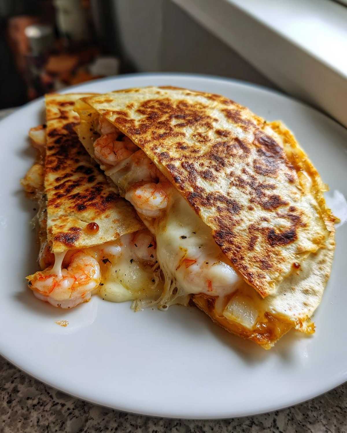 Close-up of a golden-brown shrimp quesadilla cut in half, revealing melted cheese and plump shrimp filling.