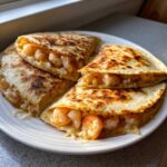 Four golden-brown quarters of a cheesy shrimp quesadilla, stuffed with pink shrimp and melted cheese.