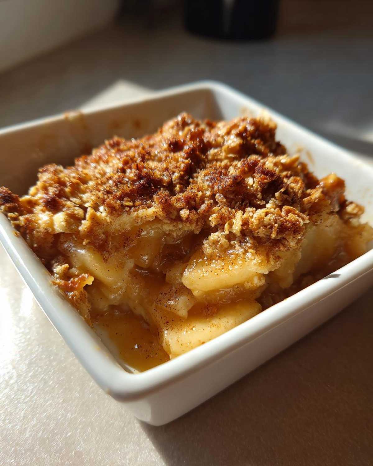 Close-up of a warm, bubbly single serving of apple crisp recipe in a white square ramekin.