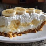 A thick slice of banana cream pie recipe showing graham cracker crust, creamy filling, and sliced bananas on top.