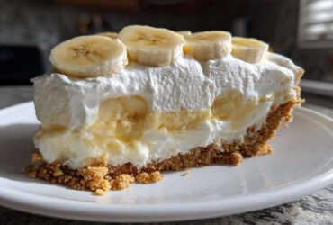A thick slice of banana cream pie recipe showing graham cracker crust, creamy filling, and sliced bananas on top.