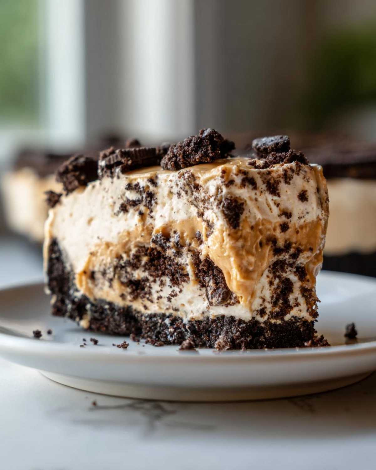 A decadent slice of no-bake peanut butter pie featuring a dark chocolate crust and creamy filling topped with cookie crumbles.