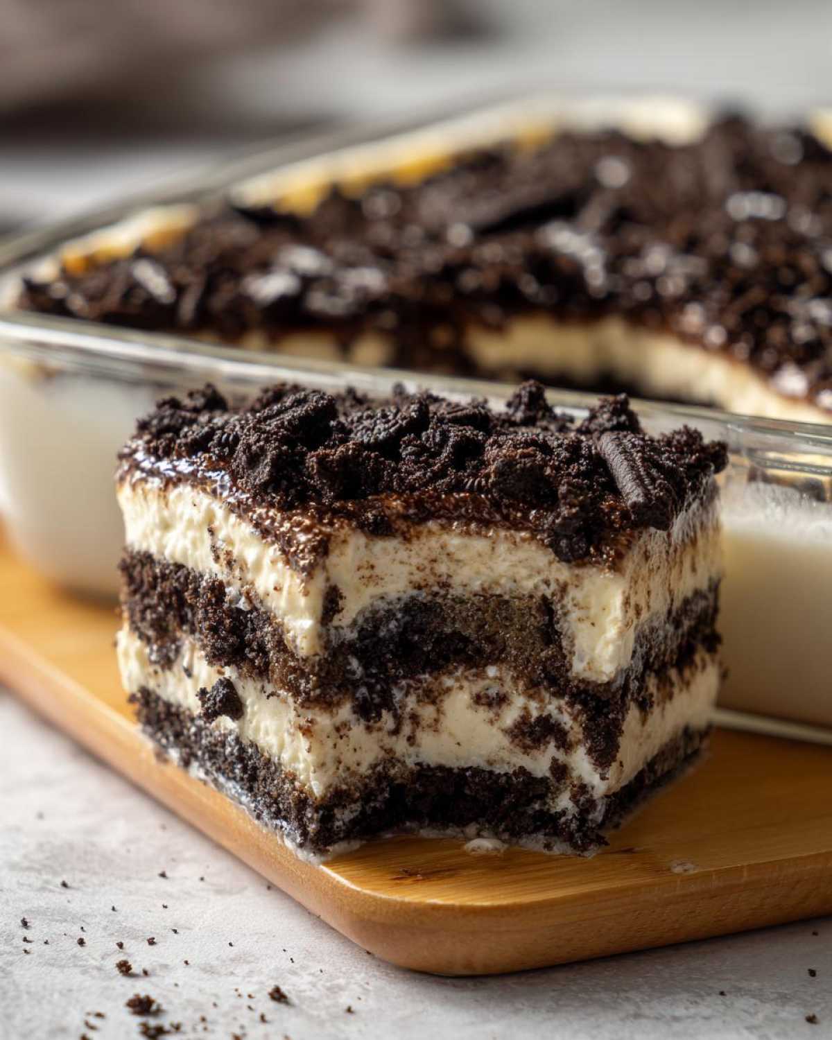 A square slice of layered dirt cake showing alternating dark chocolate cookie crumbs and white cream filling, served on a wooden board.