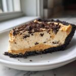 A thick slice of creamy peanut butter pie with a dark chocolate crust, topped with chocolate crumbles.